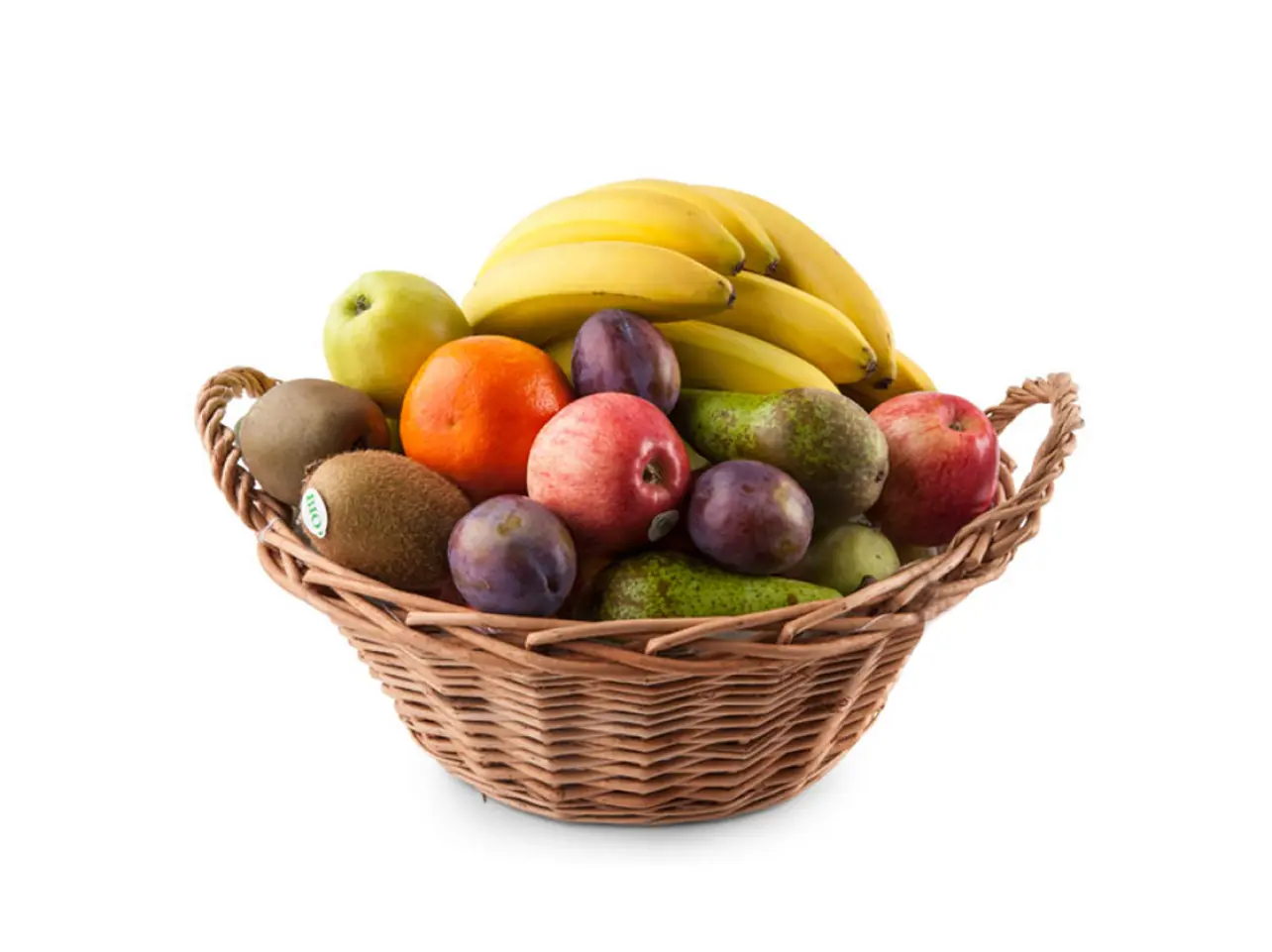 Flätad korg fylld med blandad frukt som bananer, äpplen, kiwi, plommon, apelsin och avokado mot vit bakgrund.
