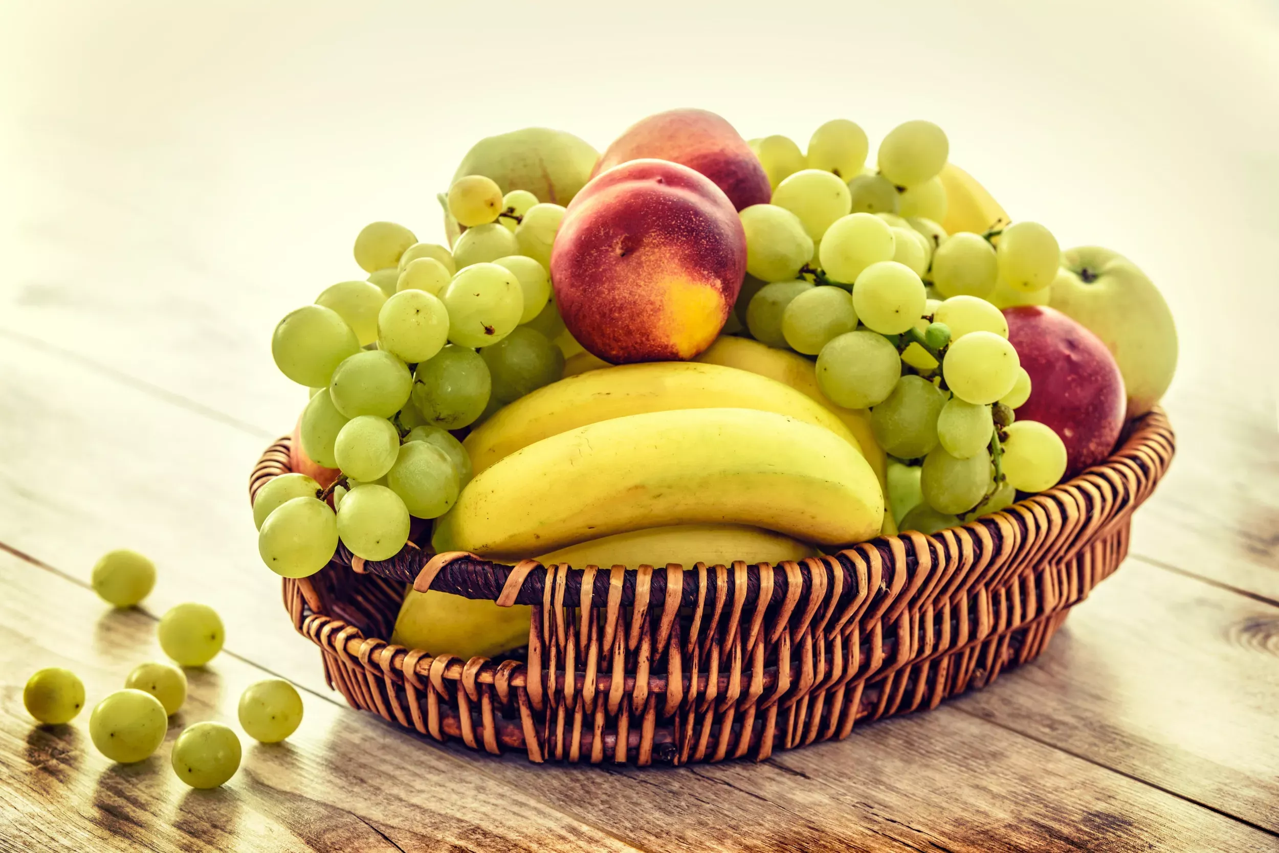 Bilden visar en fruktkorg med banan, äpple och vindruvor på ett träbord