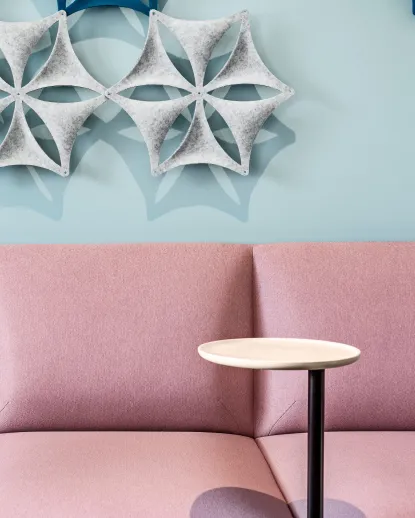 Rosa soffa med litet sidobord mot blå vägg med dekorativa former