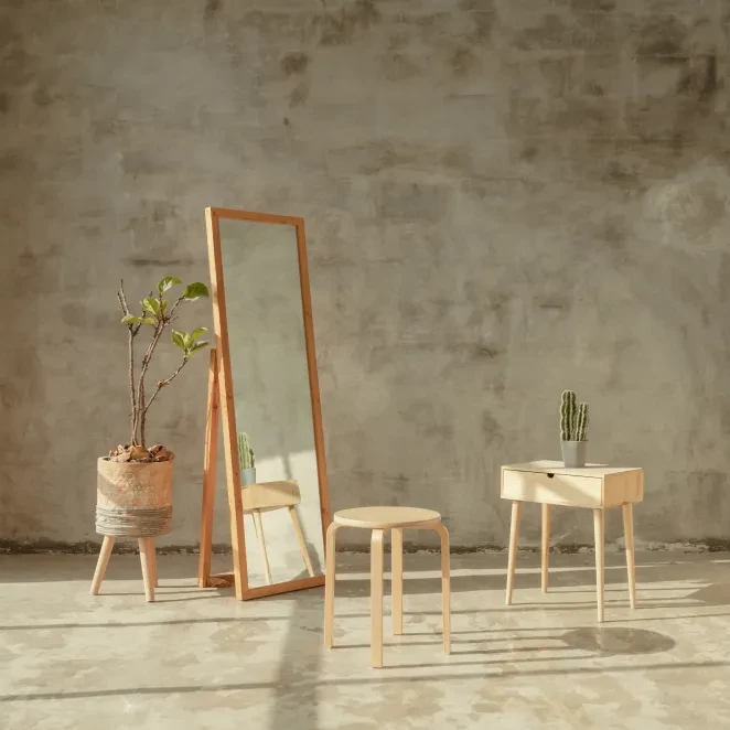 Minimalistisk inredning med spegel, pall, sidobord och växter mot betongvägg