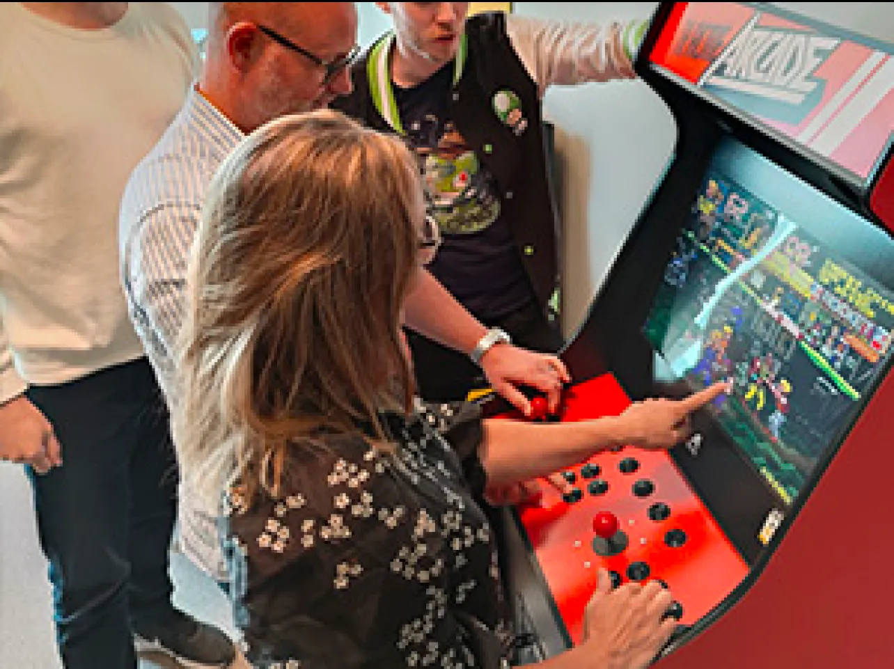 Grupp personer spelar på en arkadmaskin i en ljus kontorsmiljö