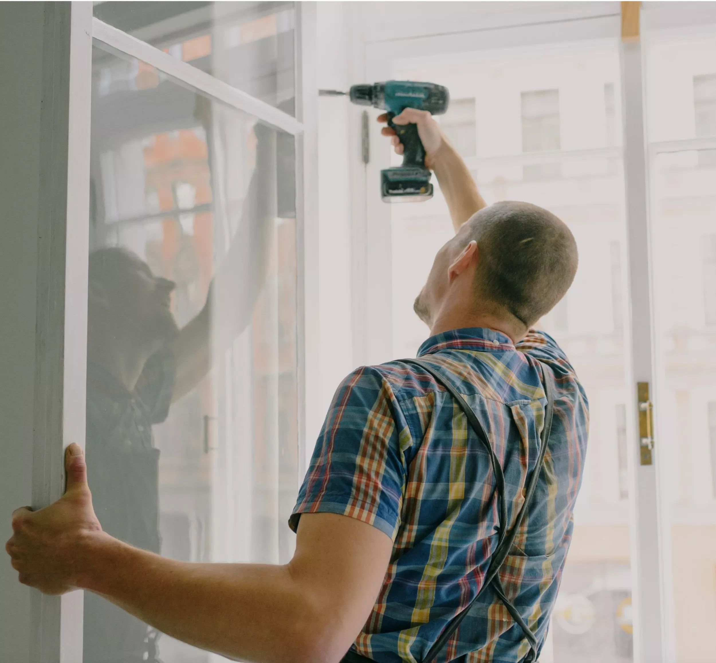 Hantverkare borrar i ramen för ett fönster medan han håller ramen på plats